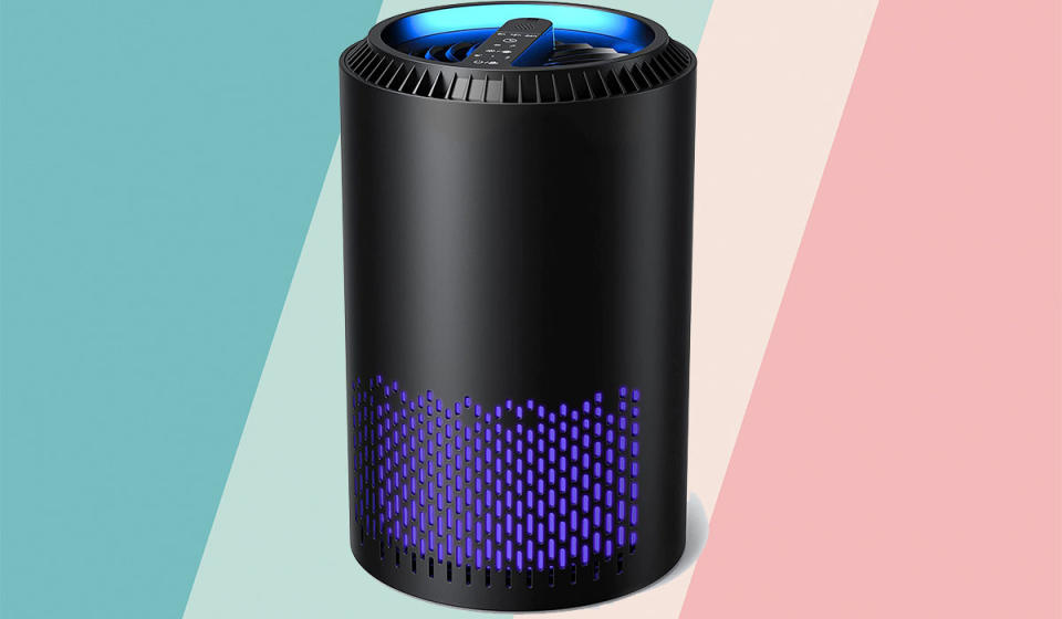 A black air purifier with purple accents atop a pastel background.