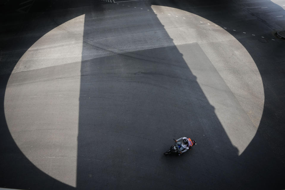 A motorcyclist drives over the shadow of train tracks in Bangkok, Thailand, Tuesday, April 9, 2024. Thailand, Cambodia and other countries in this region are celebrating with their annual water festivals as they also suffer through the global heat wave. (AP Photo/Sakchai Lalit)