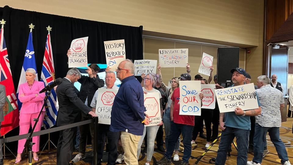 A group of about 15 people stood next to the ministers with signs calling for the stewardship fishery to be reinstated. FFAW President Greg Pretty, seen in the front wearing a blue shirt, said harvesters can't let Ottawa's decision stand.