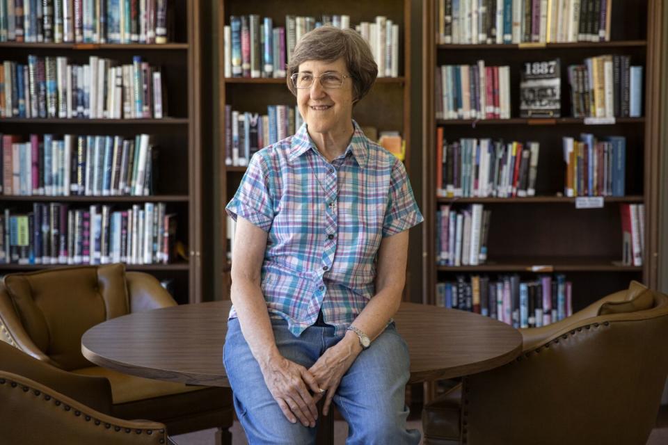 Sister Arlene Trant sitting on a small table in front of shelves of books.