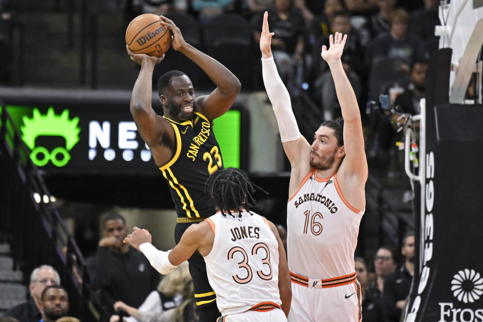 Golden State Warriors' Draymond Green (23) looks to pass as he is guarded by San Antonio Spurs' Tre Jones (33) and Cedi Osman during the first half of an NBA basketball game Sunday, March 31, 2024, in San Antonio. (AP Photo/Darren Abate)
