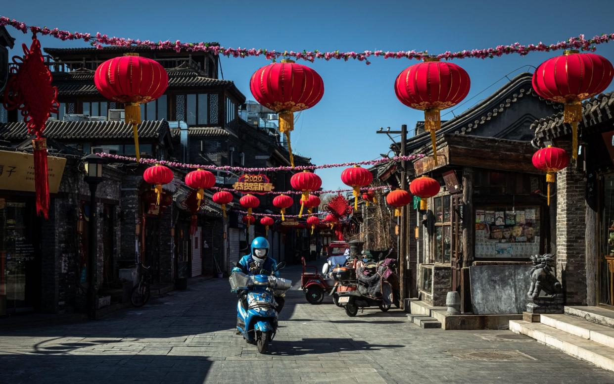 A delivery man wearing a protective face mask rides a scooter in an empty shopping street near the Houhai lake, in Beijing, China - ROMAN PILIPEY/EPA-EFE/REX