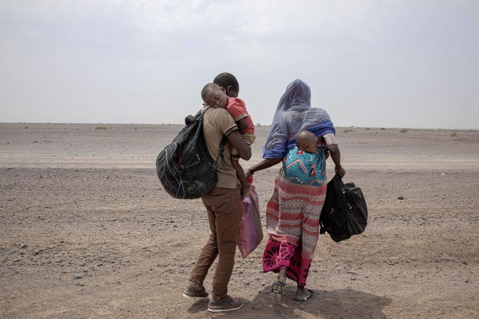 In this July 23, 2019 photo, Fatma and her husband Yacoub, migrants from Mali, carry their children as they make their way in Lahj, Yemen. Mohammed, traveled with her husband, a construction worker, and two children, through Djibouti on their way to Saudi. Once they reached the shore, they were held for several days by traffickers. (AP Photo/Nariman El-Mofty)