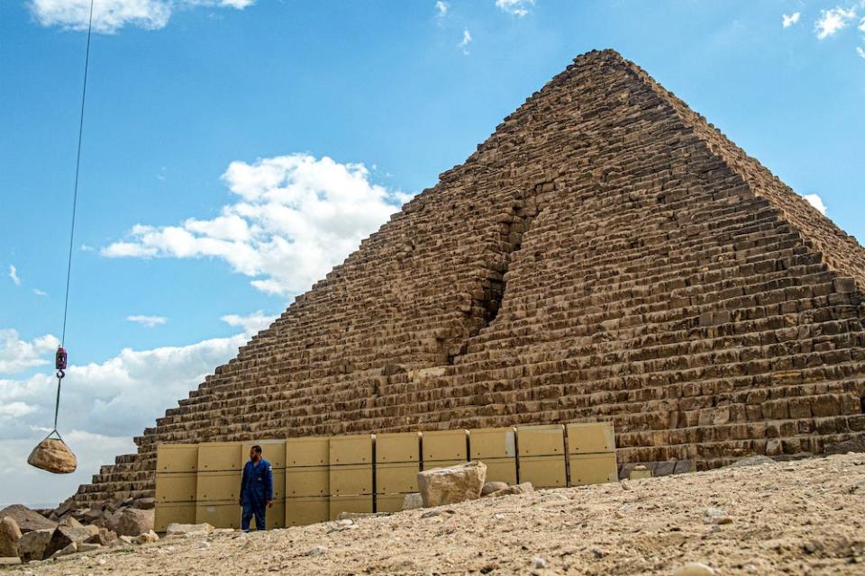 A stone is lifted by a crane during a conservation project by the base of the Pyramid of Menkaure, against a blue sky, at the Giza Pyramids west of Cairo, on January 29, 2024