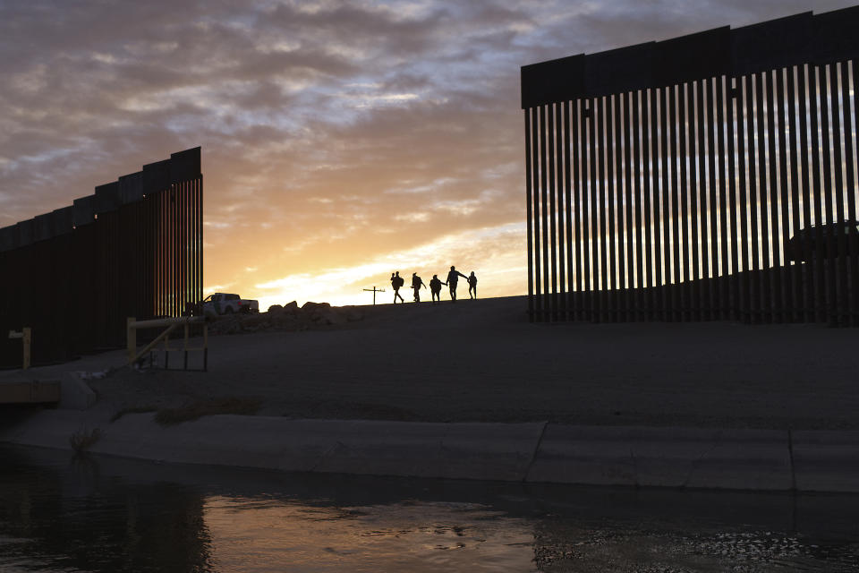 FILE - A pair of migrant families from Brazil passes through a gap in the border wall to reach the United States after crossing from Mexico in Yuma, Ariz., to seek asylum on June 10, 2021. The families are part of an influx of asylum-seekers entering the U.S. in the Yuma area from South America and other continents. Stalled negotiations for the U.S. government to pay families separated at the border during Donald Trump's presidency have brought new threats of extortion. While specific reports are isolated, widespread extortion in Central America explains why many seek asylum in the United States in the first place and some advocates fear prospects of a large payment will fuel many more threats. It is far from clear whether families will receive any money at all from the U.S. government. (AP Photo/Eugene Garcia, File)