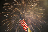 FILE - In this July 4, 2015, file photo, fireworks explode behind a United States flag during a Fourth of July celebration at State Fair Meadowlands in East Rutherford, N.J. With fewer professional celebrations on July 4, 2020, many Americans are bound to shoot off fireworks in backyards and at block parties. And they already are: Sales have been booming. (AP Photo/Julio Cortez, File)