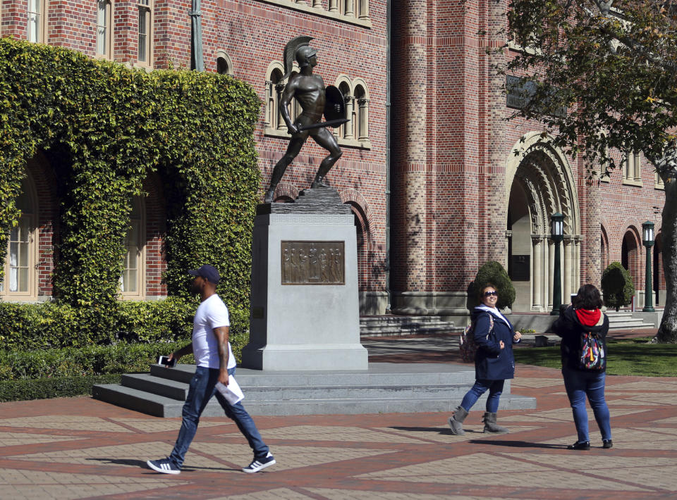 FILE - In this March 12, 2019 file photo, people pose for photos in front of the iconic Tommy Trojan statue on the campus of the University of Southern California in Los Angeles. The past year has been a bruising one for the Los Angeles university. The president who helped boost the school's endowment above $6 billion had to step down amid investigations into a medical school dean accused of smoking methamphetamine with a prostitute who overdosed, its longtime gynecologist was accused of sexual misconduct by hundreds of women he examined over decades and an assistant men's basketball coach pleaded guilty to charges stemming from an FBI probe of corruption in college basketball. (AP Photo/Reed Saxon, File)