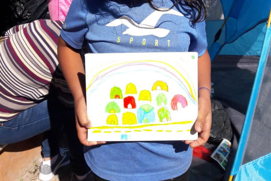 A young girl holds up her drawing of the Matamoros tent encampment where she lives. | Courtesy of Belinda Arriaga