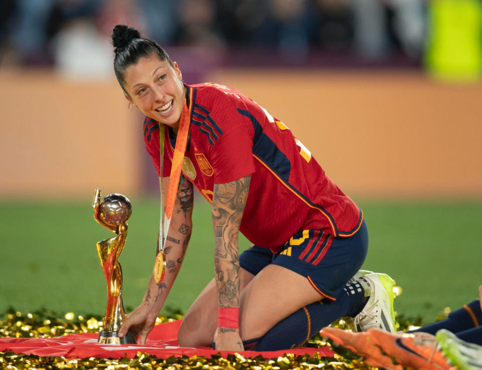 Jenni Hermoso kneels on the ground in front of the World Cup trophy
