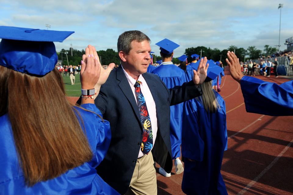 Natick High School Vice Principal Zachary Galvin high fives graduates as they enter Memorial Field for graduation, June 3, 2022.