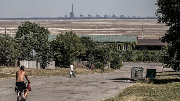 PHOTO: Residents pass along a street in Nikopol, with the Zaporizhzhia Nuclear Power Plant in the background, behind an expanse of sand exposed after the destruction of the Nova Kakhovka Dam, in Ukraine, on July 3, 2023. (The New York Times via Redux)