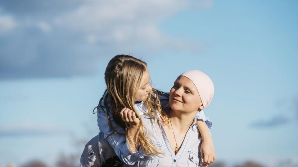 woman seen from chin to stomach holding out hands to make a heart shape to frame a pink ribbon on her white sweater