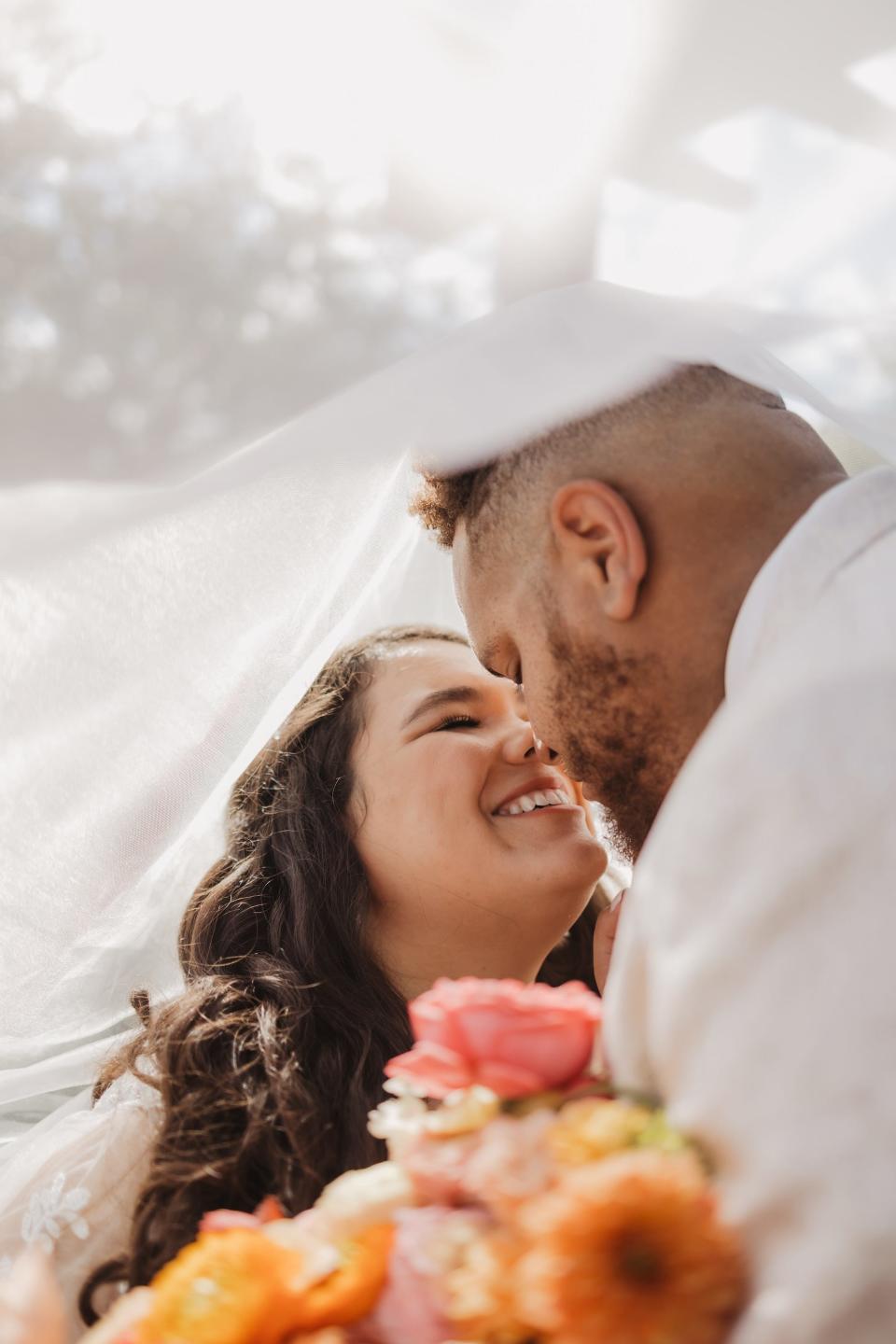 A bride and groom touch noses as they pose under her veil.