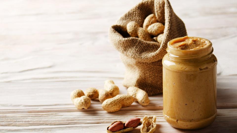 low angle view at glass mason jar with peanut butter on white wooden table with burlap sack on backside healthy eating concept