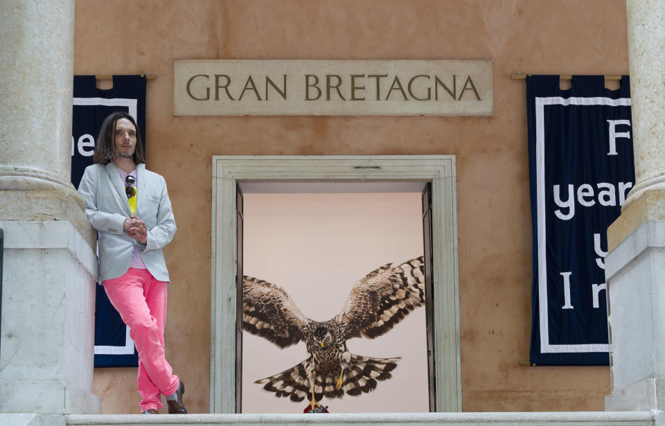 In this photo taken Wednesday, May 29, 2013, artist Jeremy Deller poses in front of the British Pavilion during a preview of the 55th edition of the Venice Biennale of Arts in Venice, northern Italy. The painting partially visible inside is Deller's 'The Sandringham Estate, Norfolk, UK 24 October 2007'. (AP Photo/Domenico Stinellis)