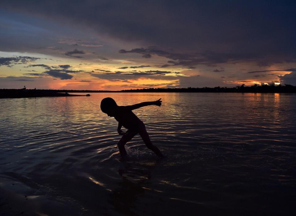 A child seen in silhouette in a river against orange skies