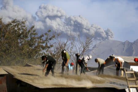 People clean an ash-covered roof of a house in Ensenada town, April 24, 2015. REUTERS/Ivan Alvarado