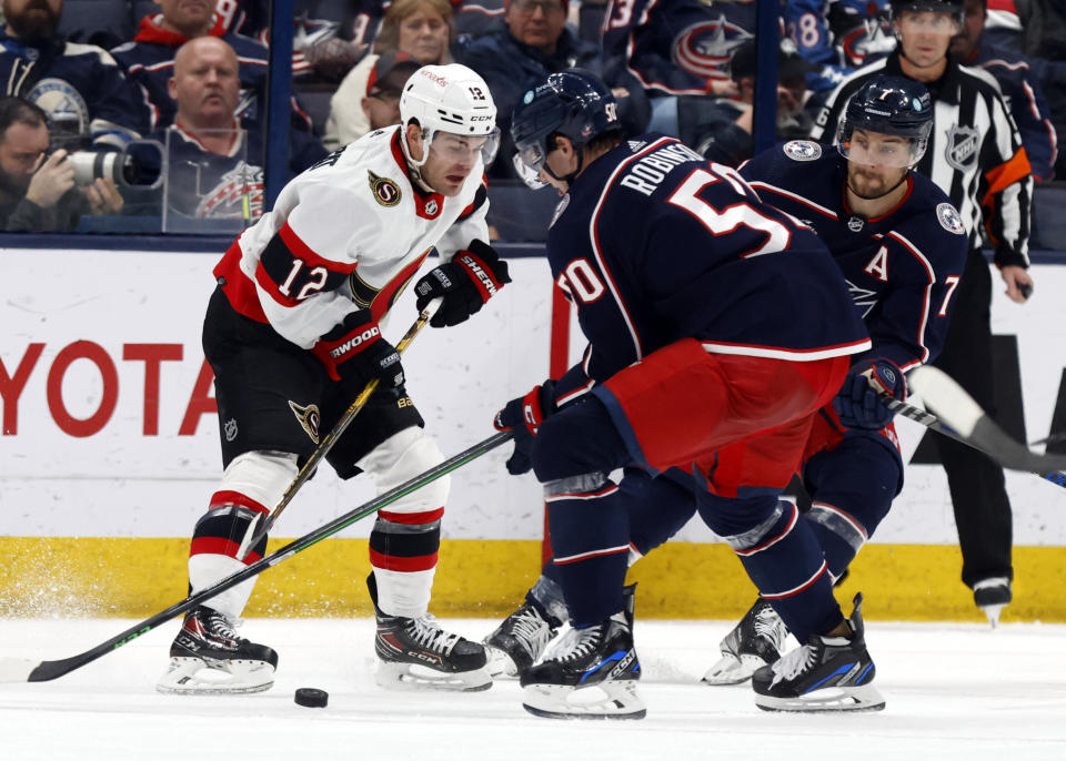 Ottawa Senators forward Alex DeBrincat, left, passes the puck in front of Columbus Blue Jackets forwards Eric Robinson, center, and Sean Kuraly during the second period of an NHL hockey game in Columbus, Ohio, Sunday, April 2, 2023. (AP Photo/Paul Vernon)