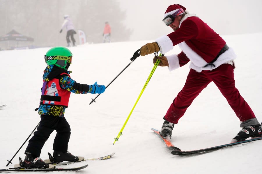 A skier dressed as Santa Claus delivers a pole to a youngster who dropped it uphill, Sunday, Dec. 10, 2023, at the Sunday River ski resort in Newry, Maine. The annual Santa Sunday event raises money for local charities. (AP Photo/Robert F. Bukaty)