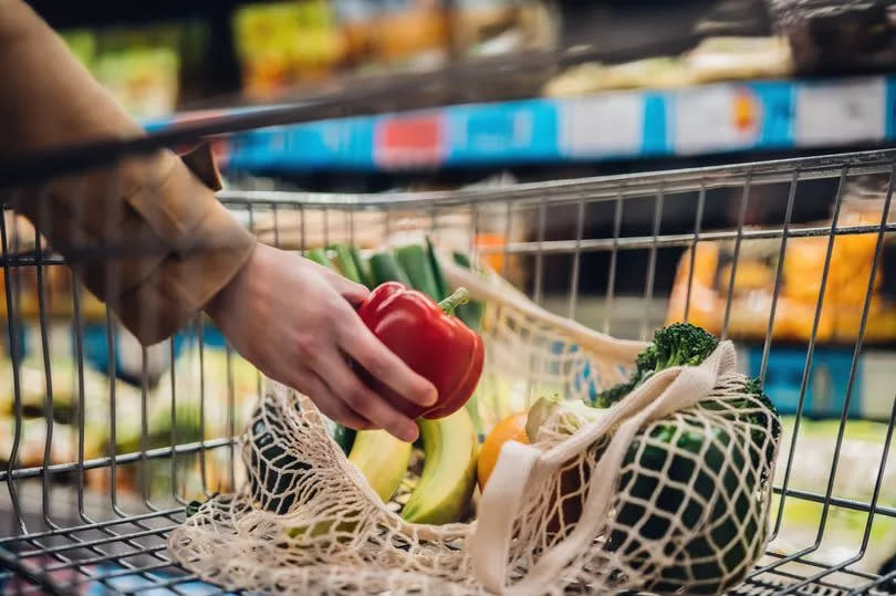 Close-up shot of female hand putting a red bell pepper into a mesh grocery bag