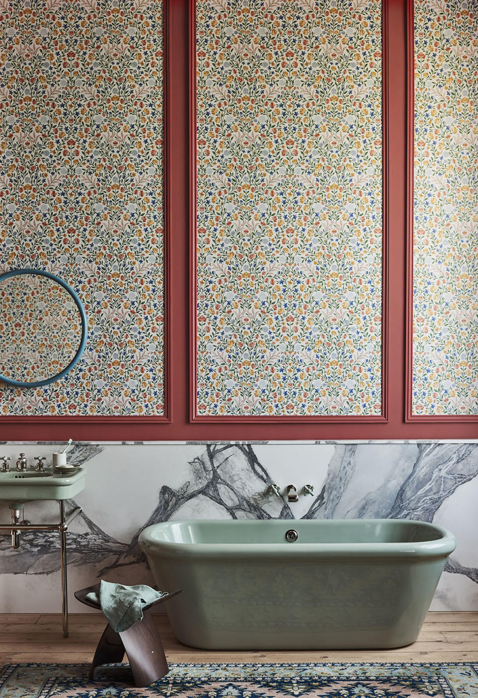 bathroom with floral wallpaper, marble backsplash, green tub, green basin, wooden floor, rug