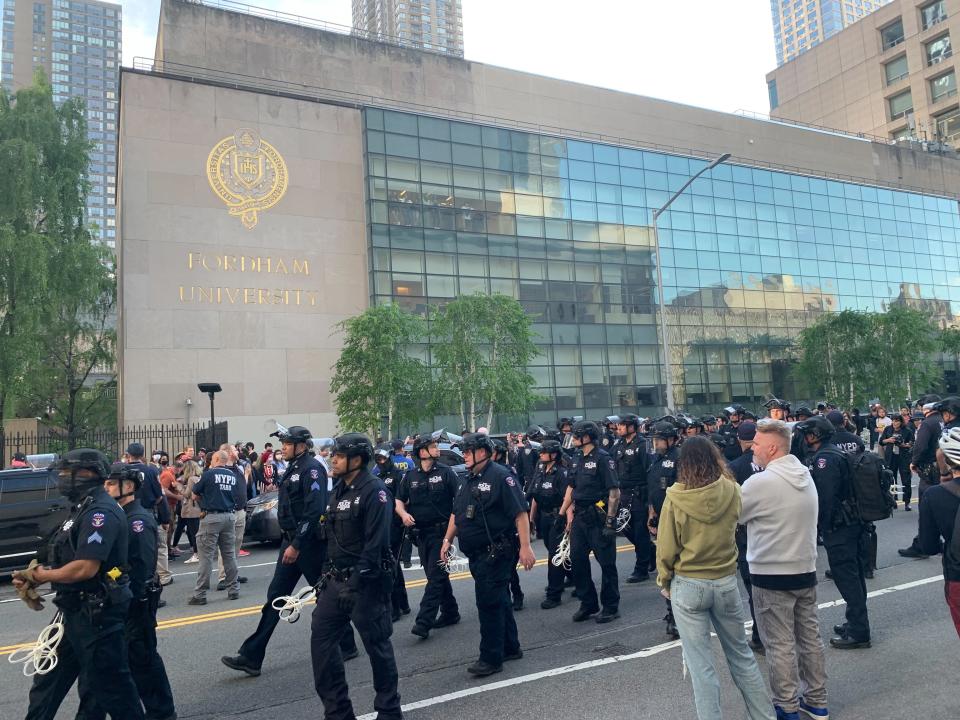 About 20 police officers walk in the street outside a Fordham building.