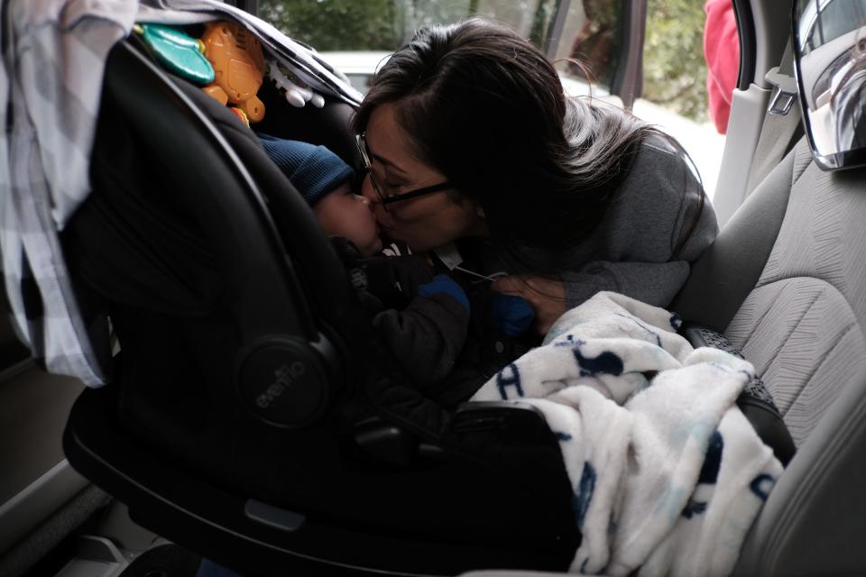 A woman leans to kiss a baby, who's in a car seat.