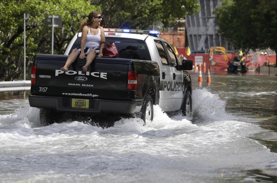 FILE- In this Sept. 30, 2015 file photo, a woman gets a ride on a police truck navigating a flooded street in Miami Beach, Fla. The street flooding was in part caused by high tides due to the lunar cycle, according to the National Weather Service. When Democratic presidential candidates meet in Miami for their first debate it'll be in what you could call the country's Ground Zero for any climate-related sea level rise. (AP Photo/Lynne Sladky, File)