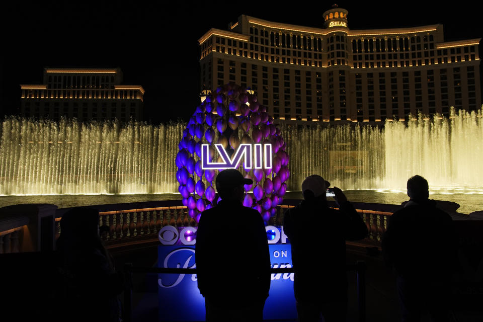 People stand by signage for the Super Bowl as the Bellagio fountains erupt along the Las Vegas Strip ahead of the Super Bowl 58 NFL football game Wednesday, Feb. 7, 2024, in Las Vegas. (AP Photo/John Locher)