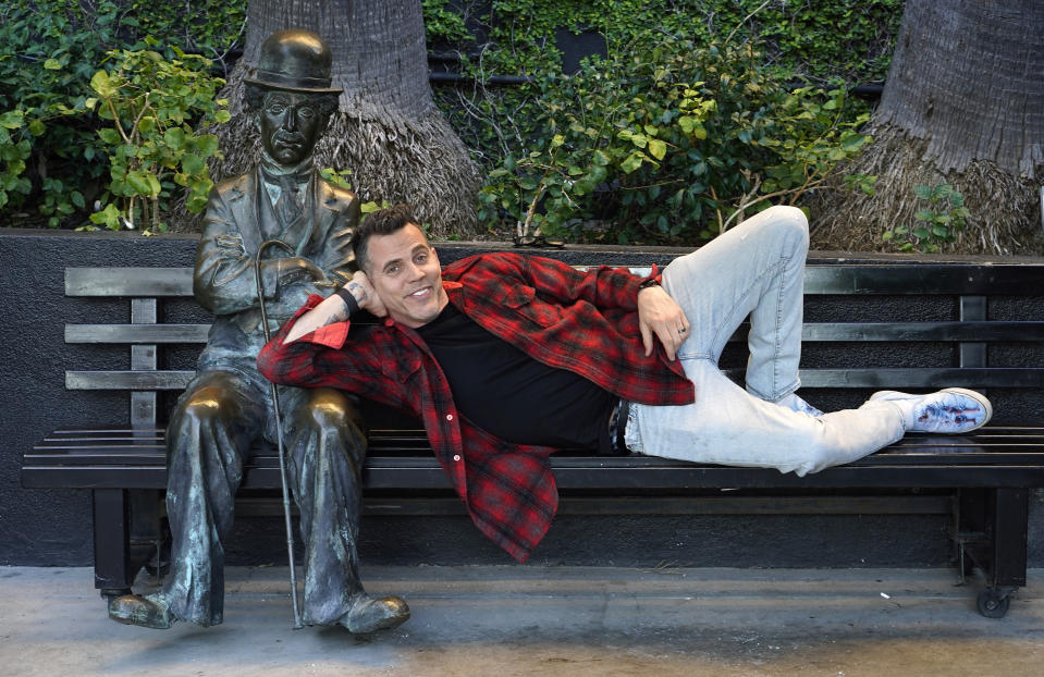 Steve-O, miembro del elenco de la película "Jackass Forever", posa junto a una estatua de Charlie Chaplin en un banco en The Hollywood Roosevelt, el jueves 27 de enero de 2022 en Los Ángeles. (AP Foto/Chris Pizzello)