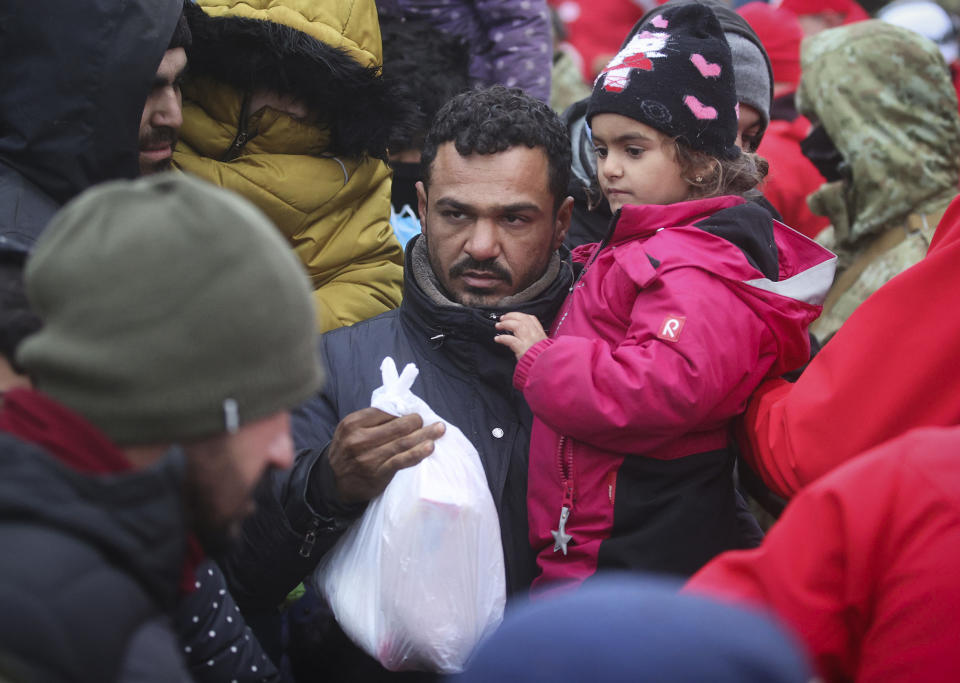 A man with a child carries a bag given as humanitarian aid as other migrants from the Middle East and elsewhere gather at the Belarus-Poland border near Grodno, Belarus, on Tuesday, Nov. 16, 2021. The EU is calling for humanitarian aid as up to 4,000 migrants are stuck in makeshift camps in freezing weather in Belarus while Poland has reinforced its border with 15,000 soldiers, in addition to border guards and police. (Leonid Shcheglov/BelTA via AP)