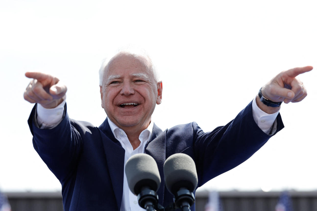 Vice presidential candidate Tim Walz gestures to the crowd as he stands at a microphone.