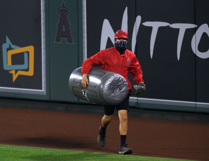 A member of the Angels grounds crew carries an inflated plastic trash can under his arm as he removes it from the field.