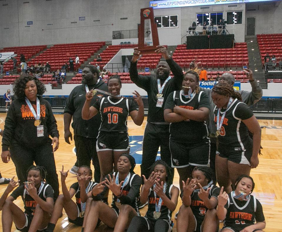 Hawthorne Head Basketball Coach Cornelius Ingram hoists the championship trophy as he and his players pose for a photo after their victory over Wildwood in the FHSAA Girls 1A Championship Basketball game at The RP Funding Center in Lakeland Wednesday. February 24, 2023. (MICHAEL WILSON)