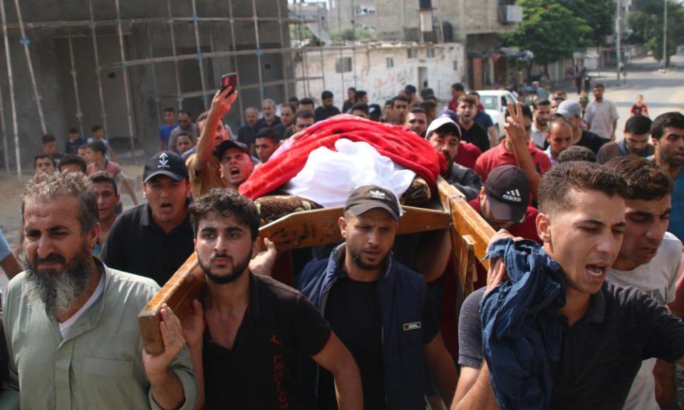 People carry a body wrapped in red and white fabric on a wooden platform 