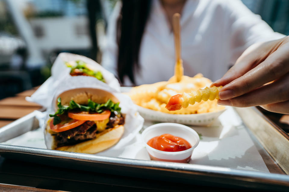 A close up of a burger and someone dipping a fry into ketchup