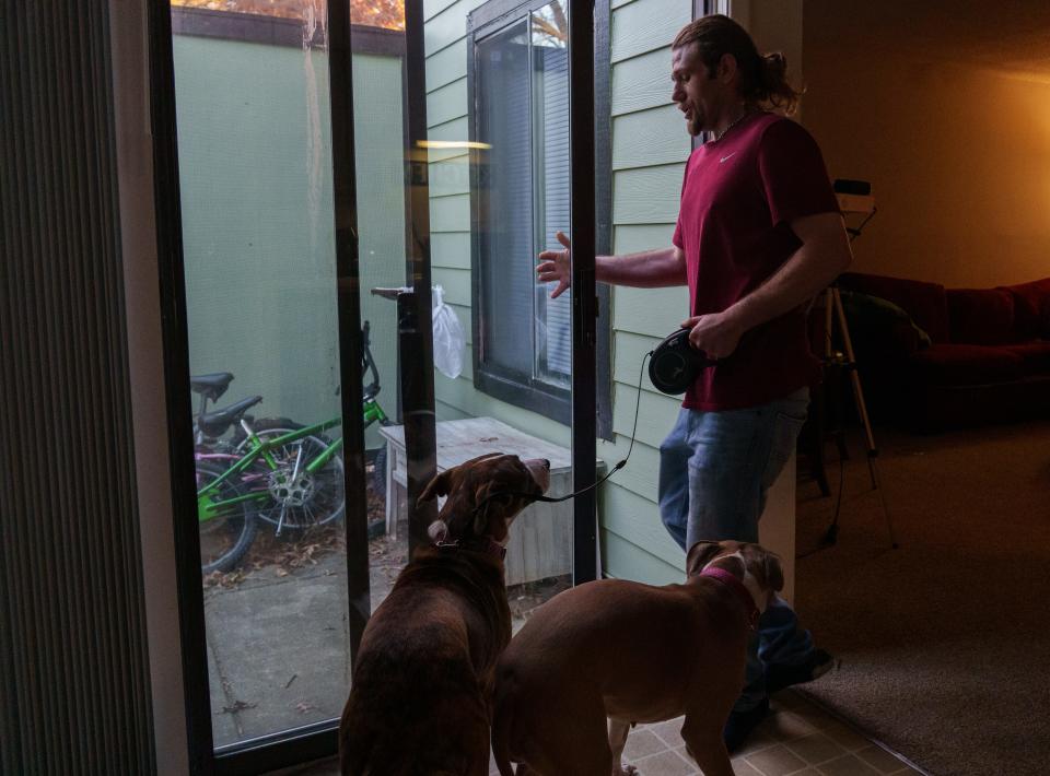 Austin Jensen opens his back sliding door Thursday, Nov. 16, 2023, to let his dogs, Riley and Carlie, outside. Jensen is waiting to start a job at UPS but has fallen behind on rent.