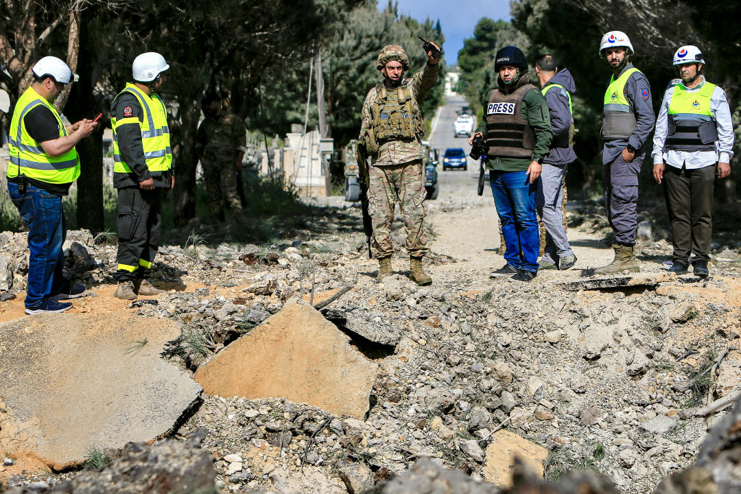 A Lebanese army soldier gestures while holding a wireless transciever as he stands with other civil defence first responders before an impact crater following an Israeli air strike that hit a road in Lebanon's southern village of Alma al-Shaab on April 15, 2024 amid ongoing cross-border tensions as fighting continues between Israel and Palestinian Hamas militants in the Gaza Strip. (Photo by AFP) (Photo by -/AFP via Getty Images)