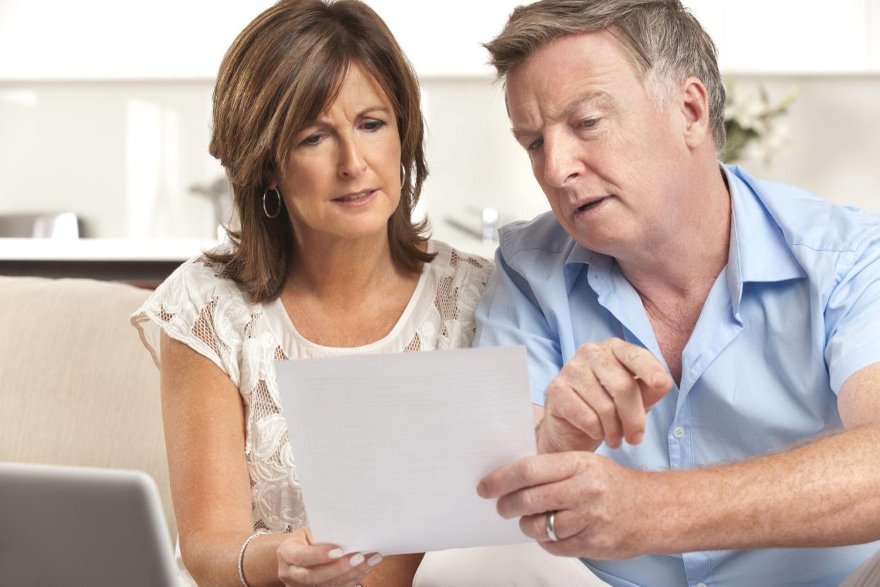 mature couple with worried expressions looking at documents and laptop