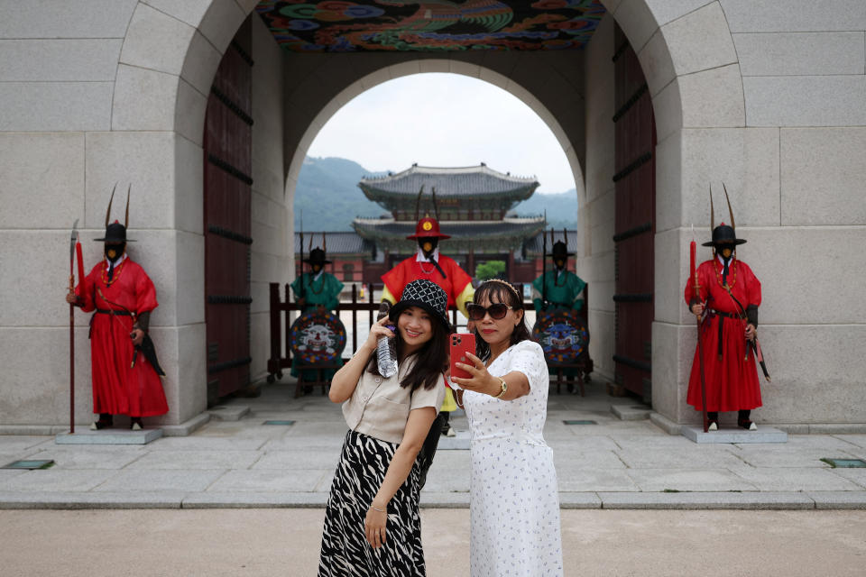 Tourists take a selfie in front of workers dressed in Korean traditional costumes at Gyeongbok Palace in central Seoul, South Korea, July 8, 2022. REUTERS/Kim Hong-Ji