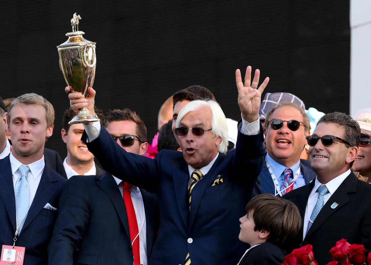 Trainer Bob Baffert hoists the trophy in the winner's circle after Victor Espinoza rode American Pharoah to win the Kentucky Derby at Churchill Downs. He's holding up four fingers to symbolize it marked his fourth Kentucky Derby victory.