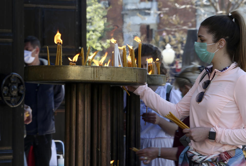 In this Thursday, April 16, 2020, photo, a young woman wearing a face mask to protect herself from the coronavirus lights candles in front of St. Clement Christian Orthodox Church in Skopje, North Macedonia. For Orthodox Christians, this is normally a time of reflection, communal mourning and then joyful release, of centuries-old ceremonies steeped in symbolism and tradition. But this year, Easter - by far the most significant religious holiday for the world's roughly 300 million Orthodox - has essentially been cancelled. (AP Photo/Boris Grdanoski)