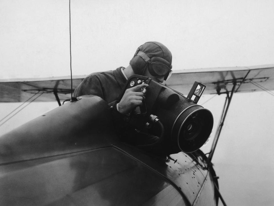 An airman sitting in the cockpit of a plane using a Fairchild F 14 rapid-action, automatic military aerial camera in 1935.