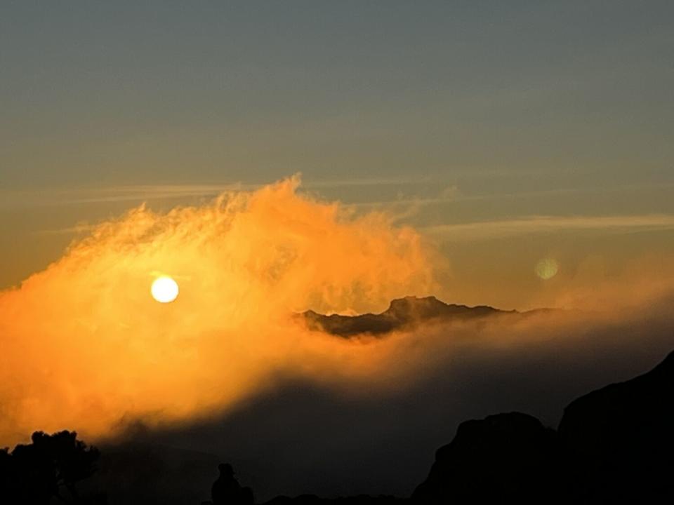 The sun illuminates clouds shrouding mountain peaks