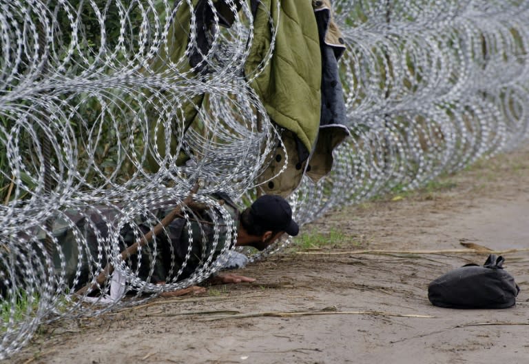 A migrant man creeps under the metal fence near the Hungarian village of Roszke, at the border with Serbia, August 26, 2015