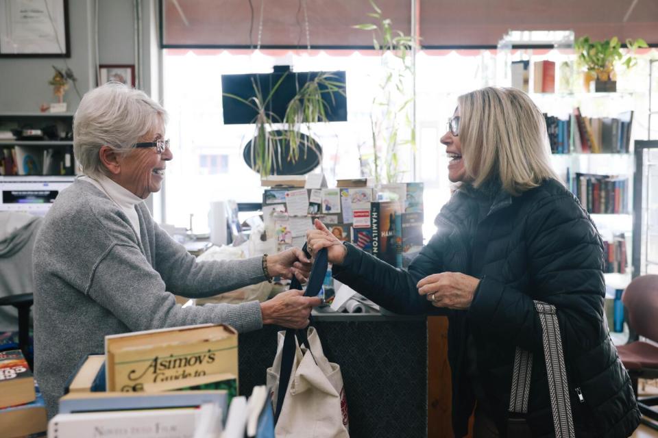 A woman hands another woman a bag in a bookstore.