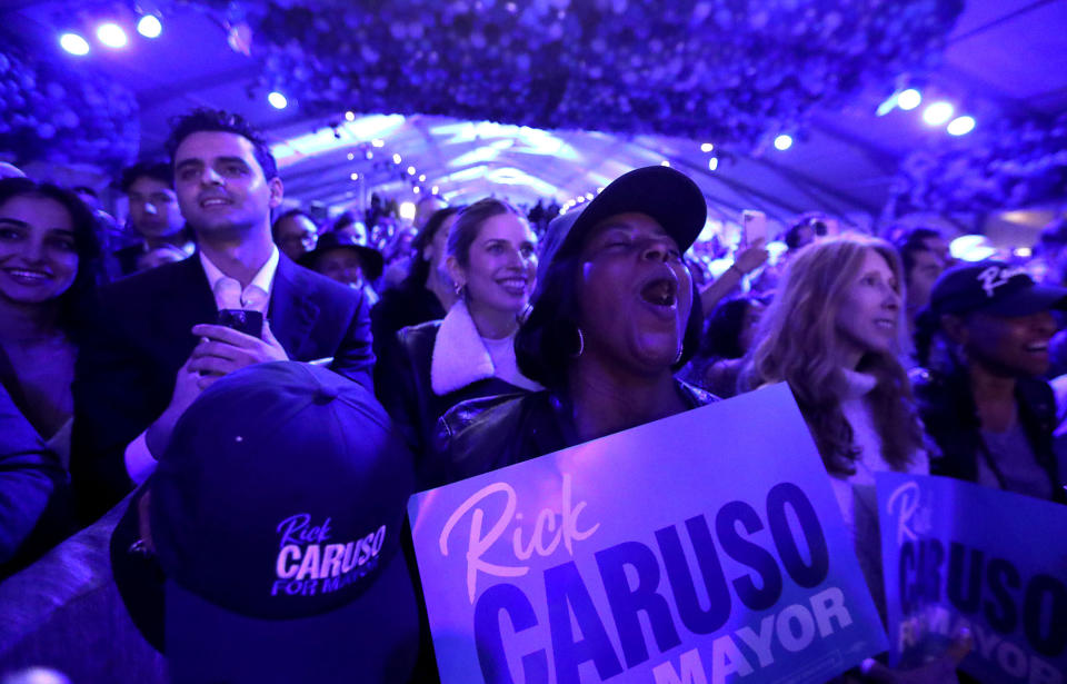 Supporters, one wearing a baseball cap and one with a poster, both carrying his name, cheer Rick Caruso.