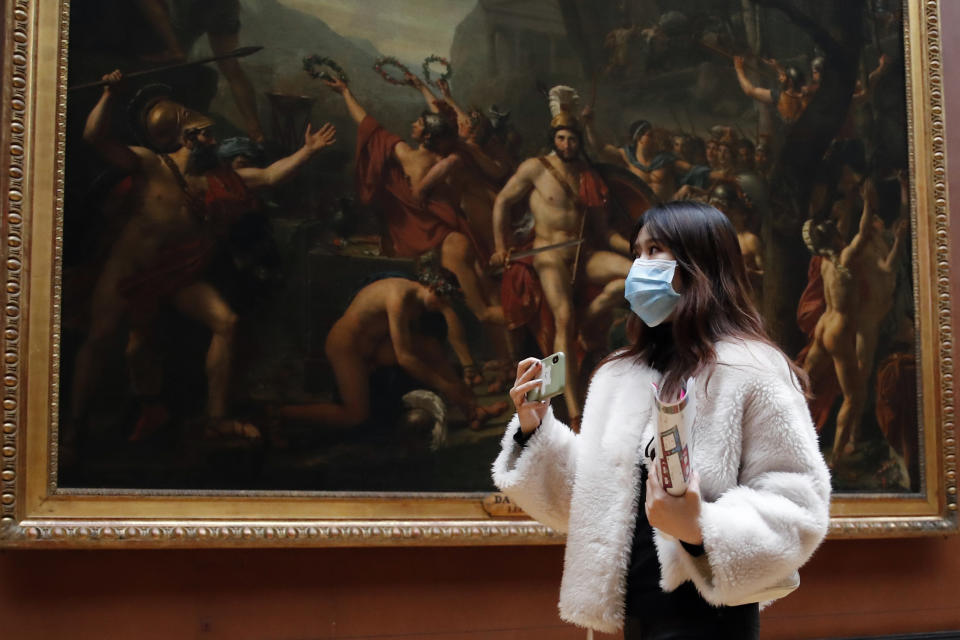 Masked tourist walks by an oil on canvas of 1814 entitled Leonidas at Thermopylae, by Jacques Louis David, at the Louvre Museum in Paris, Thursday, March 5, 2020. With the COVID-19 virus taking firmer hold in Europe, the continent is facing the same complications seen in Asia weeks ago. (AP Photo/Francois Mori)