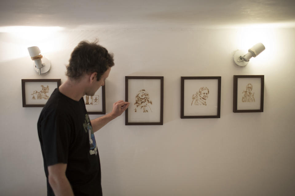 Brazilian artist Fernando de la Rocque stands in front of some of their pieces of art at the La Cucharacha, a small alternative gallery in the stylish, in Rio de Janeiro, Brazil, Monday Aug.  20, 2012. Some of Rocque's pot-stained prints are being sold for $2,500 each. It takes him a week to complete a single print blowing about five joints' worth of smoke onto a paper daily.  (AP Photo/Felipe Dana)