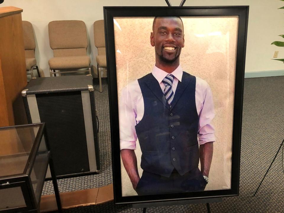 A portrait of Tyre Nichols, a Black man wearing a suit, in a black frame